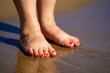 Wet female feet with red nail polish on the beach.