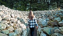 Beautiful Woman Visiting Clava Cairns Each Enclosed By Stone Circles In Inverness. A Female Tourist Explores An Ancient Burial Site, A Type Of Bronze Age Circular Chamber Tomb Cairn In Scotland.