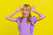 Cheerful funny bully young cute girl showing tongue making faces at camera, fooling around, joking, aping with silly face, teasing. Preteen blonde child kid on yellow background. Little children