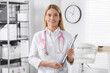 Doctor with stethoscope, clipboard and pink ribbon indoors. Breast cancer awareness