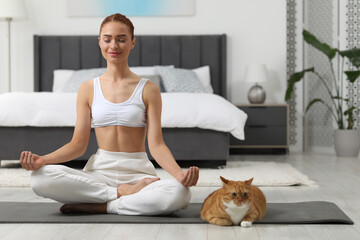 Poster - Beautiful woman with cute red cat practicing yoga on mat at home