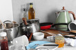 Many dirty utensils, cookware and dishware on countertop in messy kitchen