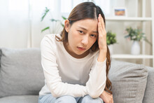 Dizzy Asian Young Woman, Girl Headache Or Migraine Pain Suffering From Vertigo While Sitting On Couch In Living Room At Home, Holding Head With Hand, Health Problem Of Brain Or Inner Ear Not Balance.