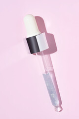 Wall Mural - close up of pipette with pouring liquid serum and shadows on pink background. Trendy cosmetics shot with hard shadows.