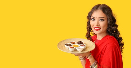 Sticker - Beautiful Indian woman holding plate with different spices on yellow background with space for text