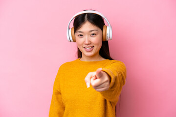 Wall Mural - Young Chinese woman isolated on pink background listening music and pointing to the front