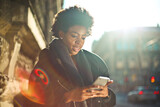 Fototapeta Krajobraz - young black woman uses a smartphone on the street