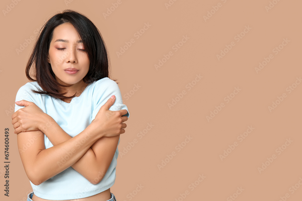 Young Asian woman hugging herself on brown background