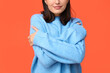 Young woman hugging herself on orange background, closeup