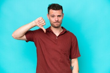 Wall Mural - Young caucasian handsome man isolated on blue background showing thumb down with negative expression