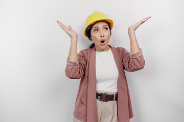 Shocked Asian woman employee wearing safety helmet pointing at the copy space on top of her, isolated by white background