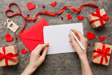 Wall Mural - top view photo of valentine day decor female hands holding letter with envelope, small gift box and heart decoration on isolated pastel colored background with empty space