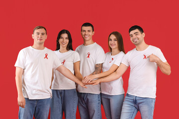 Sticker - Group of young people with red ribbons putting hands together on color background. World AIDS day concept