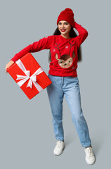 Sticker - Beautiful young woman in Christmas sweater with gift box on grey background