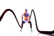 Shirtless, sportive, muscular young man training with battle rope against white studio background in neon light. Strong hands. Concept of sport, active and healthy lifestyle, body care, fitness
