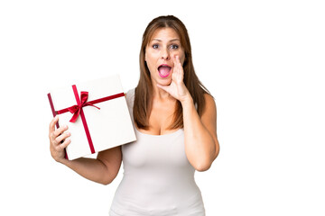 Canvas Print - Middle age caucasian woman holding a gift over isolated background shouting with mouth wide open