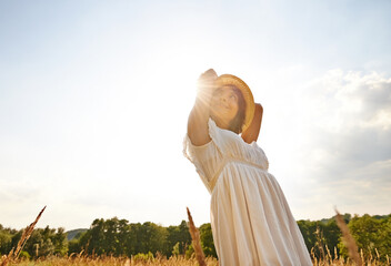 Wall Mural - Thinking, relax and woman with sunshine, countryside and nature with grass, vacation and outdoor. Person, holiday and girl with lens flare, dress and sustainability with confidence, energy or freedom