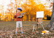 adorable kid boy with beret painting in park on old vintage rusted easel.preschool child holding brush,smiling creating.autumn fall season,amazing nature.palette with mixed colors in artist hand.