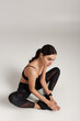 © LIGHTFIELD STUDIOS - pretty sportswoman in black active wear with fitness tracker on wrist sitting on grey backdrop