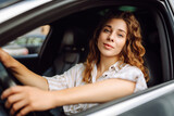 Fototapeta  - Smiling woman driving her car. Portrait of a stylish woman in casual clothes driving a car. Car travel concept.