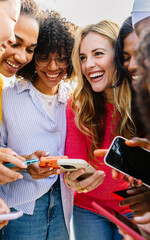 Happy female group using mobile phone together outdoors. Diverse women friends laughing while watching funny social media content on cellphone network app. Friendship and technology lifestyle concept