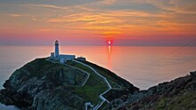 Timelapse Over South Stack Lighthouse At Golden Sunset In North-west Coast Of Holy Island, Wales. Hyperlapse Over Lighthouse With Steps And Picturesque Footbridge Over The Wild Atlantic Ocean.