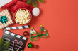 Christmas movie night and party concept with  popcorn, Santa hat, decorations and movie clapper board on red background. Top view, flat lay