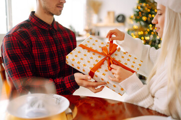 Wall Mural - Beautiful couple in love near the Christmas tree, celebrating the exchange of gifts, spending time together. Holiday concept.