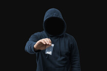 Faceless Man In A Hood Holds Transparent Plastic Bag With White Pills Hard Drugs On Dark Background, Anonymous Drug Dealer Or Gangster Sells Narcotics