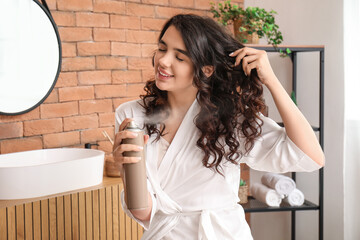 Wall Mural - Pretty young woman applying hair spray on her curly hair in bathroom