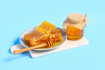 Jar of sweet honey and plate with combs on blue background