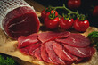 Whole and sliced bresaola on paper on a cutting board with tomatoes