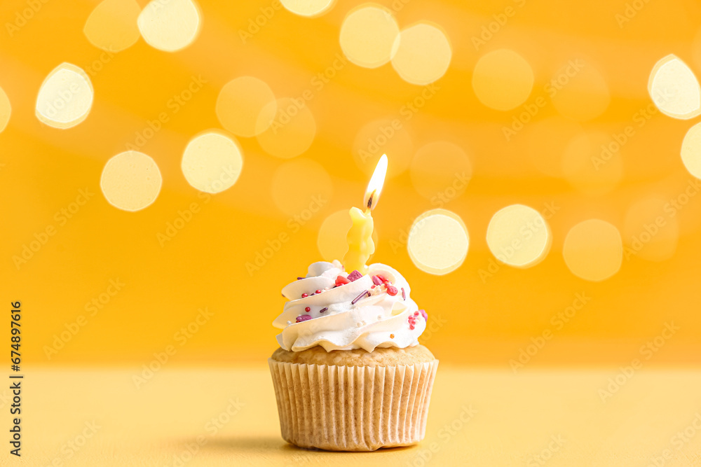 Tasty Birthday cupcake with burning candle on yellow table against blurred lights