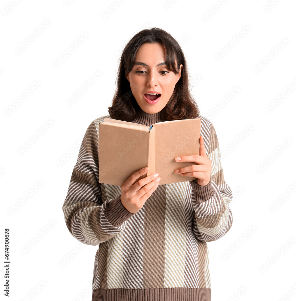 Surprised young woman in warm sweater reading book on white background