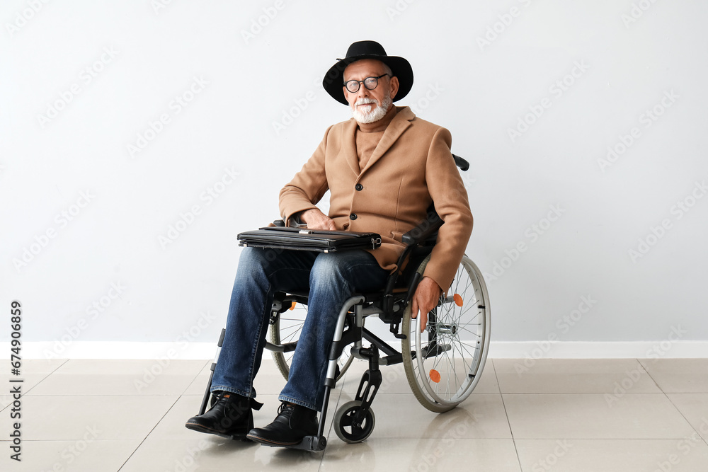 Senior man in wheelchair near light wall