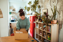Young Woman Opening And Unpacking Cardboard Box At Home