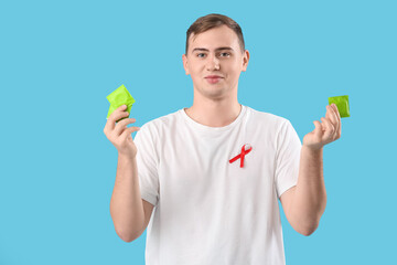 Sticker - Handsome young man with red ribbon and condoms on blue background. World AIDS day concept