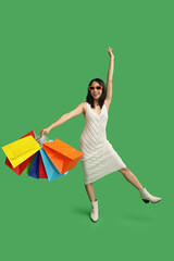 Wall Mural - Young Asian woman in sunglasses with shopping bags on green background