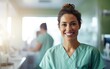 © piai - A female nurse wearing green scrubs smiling at a patient behind a counter in a bright medical laboratory