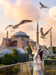 Lifestyle, Asian woman tourist feeding seagulls at view point in vacation. There is a Hagia Sophia or Ayasofya Mosque in background in a blur. Popular tourist destination. Istanbul, Turkiye, Turkey
