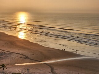 Wall Mural - Sunset reflecting over the sea with people walking on the beach sand