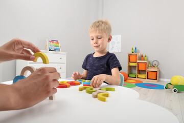 Canvas Print - Motor skills development. Mother helping her son to play with colorful wooden arcs at white table in room