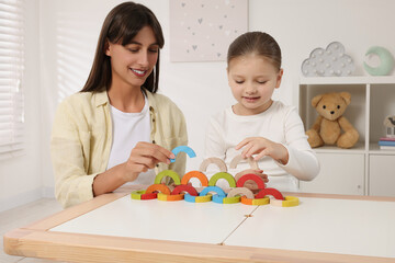 Poster - Motor skills development. Mother helping her daughter to play with colorful wooden arcs at white table in room