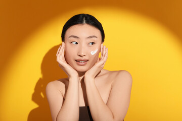 Wall Mural - Beautiful young woman in sunlight with sun protection cream on her face against orange background