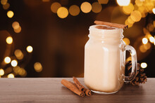 Delicious Eggnog In Mason Jar On Wooden Table Against Blurred Christmas Lights, Space For Text