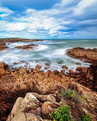 Poster - Rocky shoreline surrounded by a bright blue sky and reflecting on the shallow waters