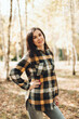 © Mila - A beautiful girl in jeans and a plaid shirt walks in a birch grove. Portraits of a brunette girl in nature, in the autumn forest