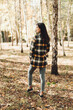 © Mila - A beautiful girl in jeans and a plaid shirt walks in a birch grove. Portraits of a brunette girl in nature, in the autumn forest
