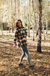 © Mila - A beautiful girl in jeans and a plaid shirt walks in a birch grove. Portraits of a brunette girl in nature, in the autumn forest