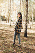 © Mila - A beautiful girl in jeans and a plaid shirt walks in a birch grove. Portraits of a brunette girl in nature, in the autumn forest